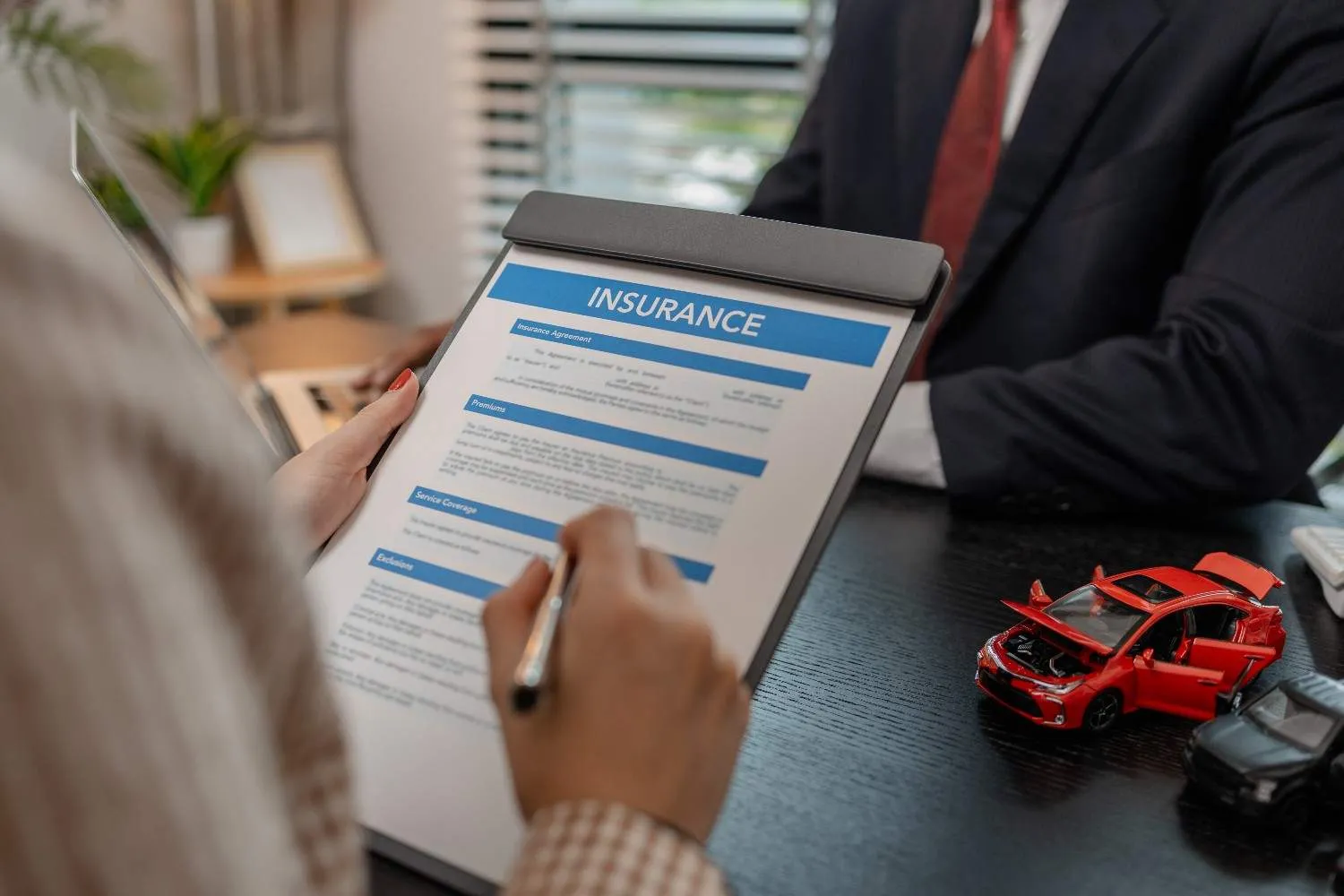 Auto insurance agreement being reviewed at a desk beside two model cars
