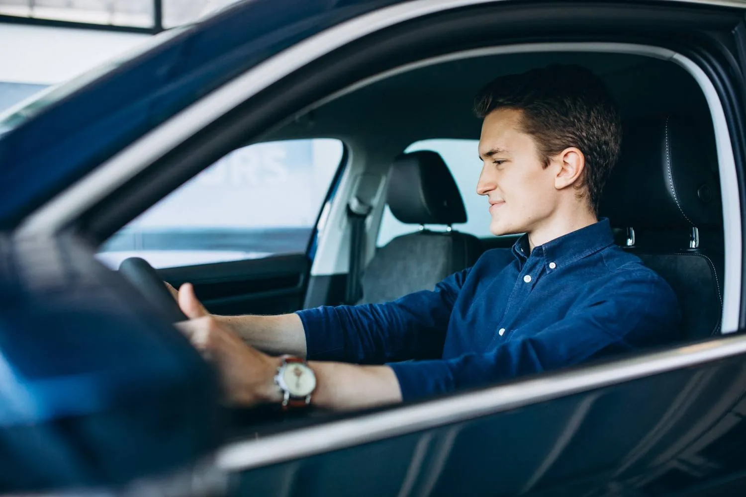 Driver at the wheel of a parked car with one hand resting on the steering wheel